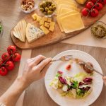 Overhead view of a cheese platter with fresh salad and juice, perfect for a gourmet lunch setting.